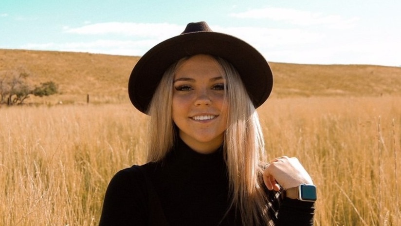 A woman wearing a black hat smiling with a backdrop of