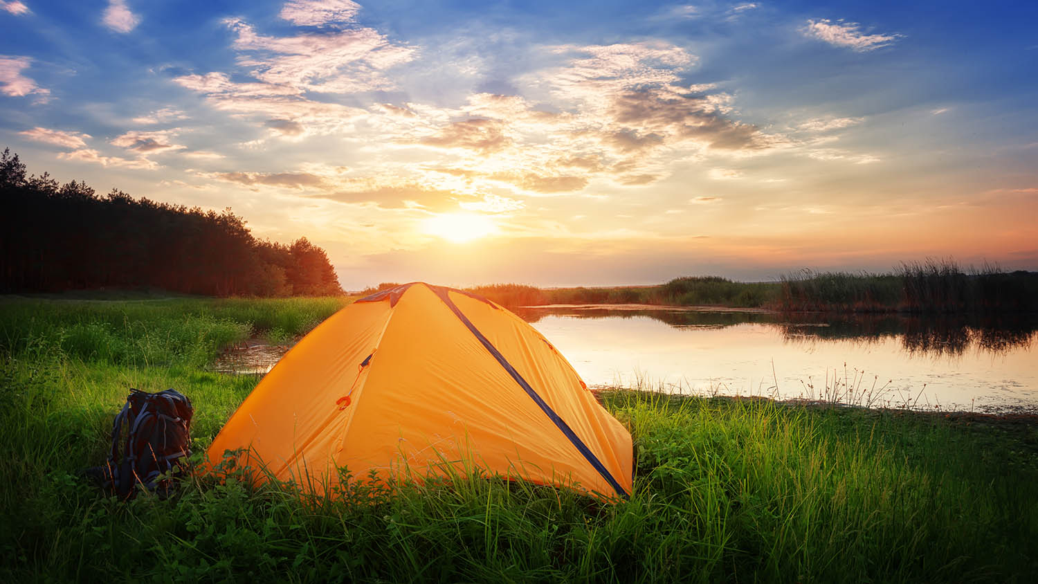 sunset photo of a tent and backpack in long grass next to a small body of water