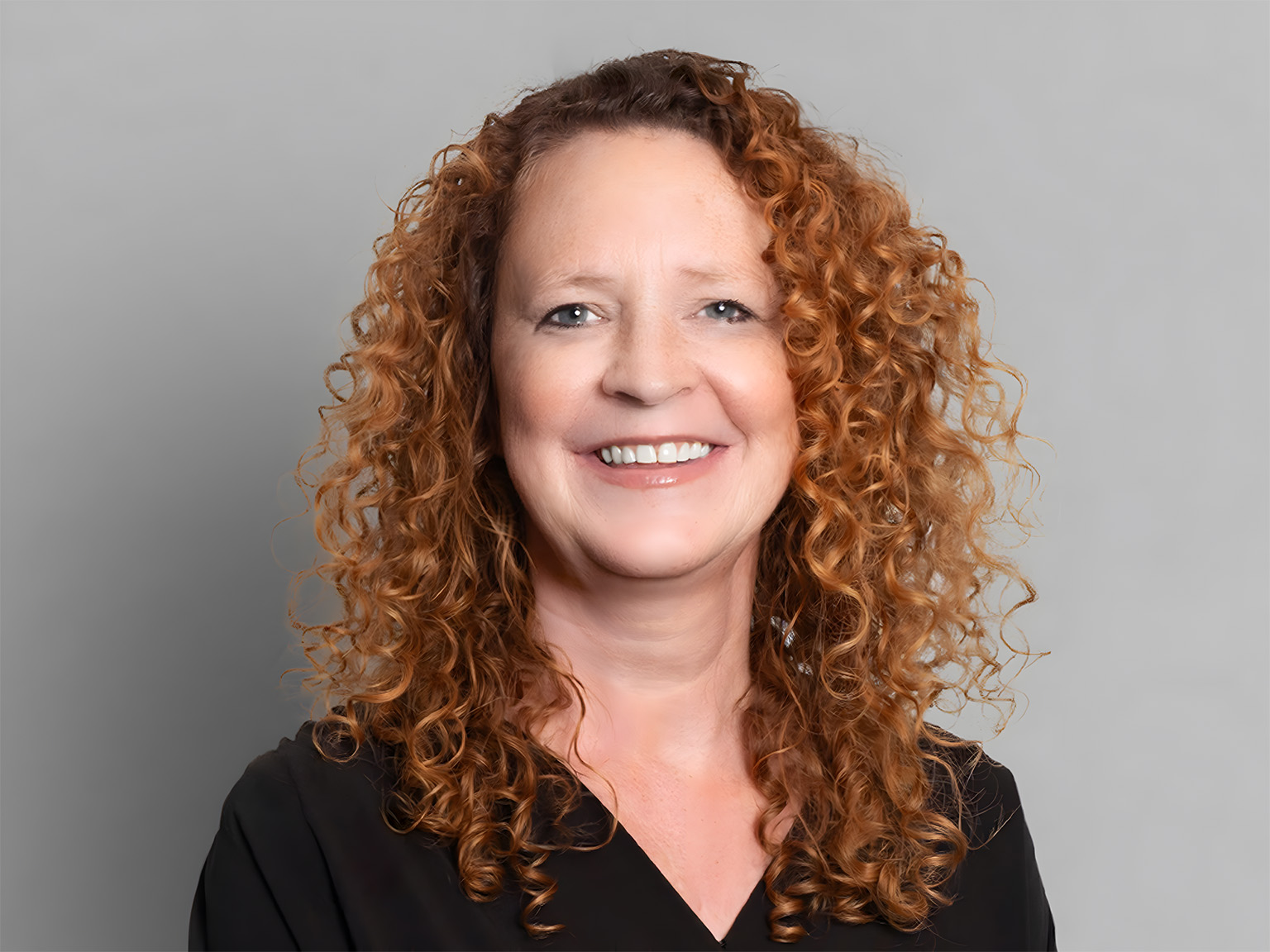 A smiling woman wearing black with a plain backdrop.